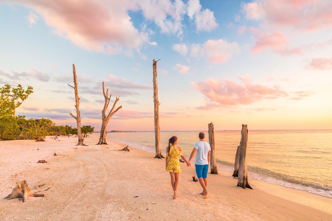 Couple walking on beach at sunset romantic travel getaway, idyllic Florida destination, Lovers Key State Park in the gulf of Mexico. Woman and man holding hands relaxing. Southwest Florida.