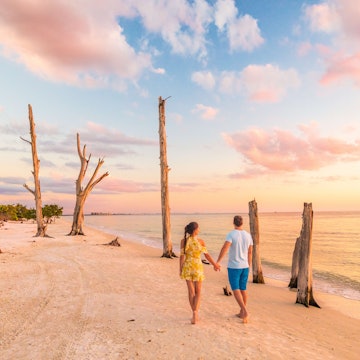Couple walking on beach at sunset romantic travel getaway, idyllic Florida destination, Lovers Key State Park in the gulf of Mexico. Woman and man holding hands relaxing. Southwest Florida.