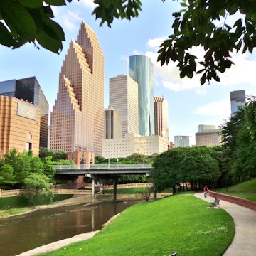 Wide shot of Houston's modern skyline and paved bicycle/walking path in Buffalo Bayou Park on a summer afternoon