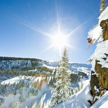 Skier jumping cliff on sunny winter day.