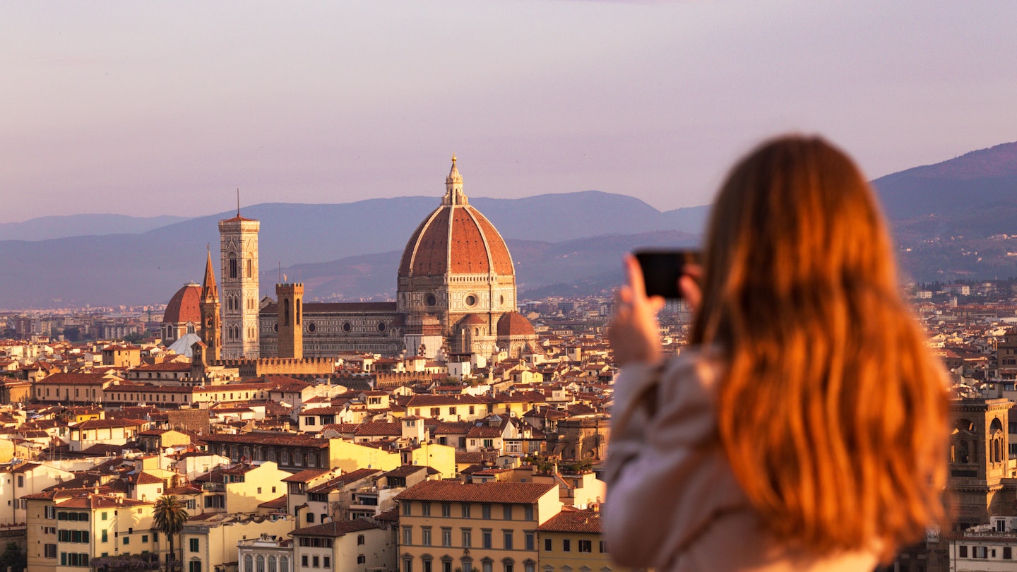 A woman taking a photo of the Florence skyline at sunset.