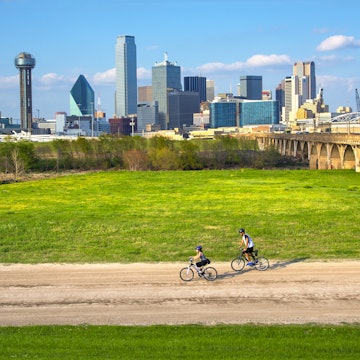 Cyclists on the bike trail in Trinity River Park with a backdrop of the Dallas skyline