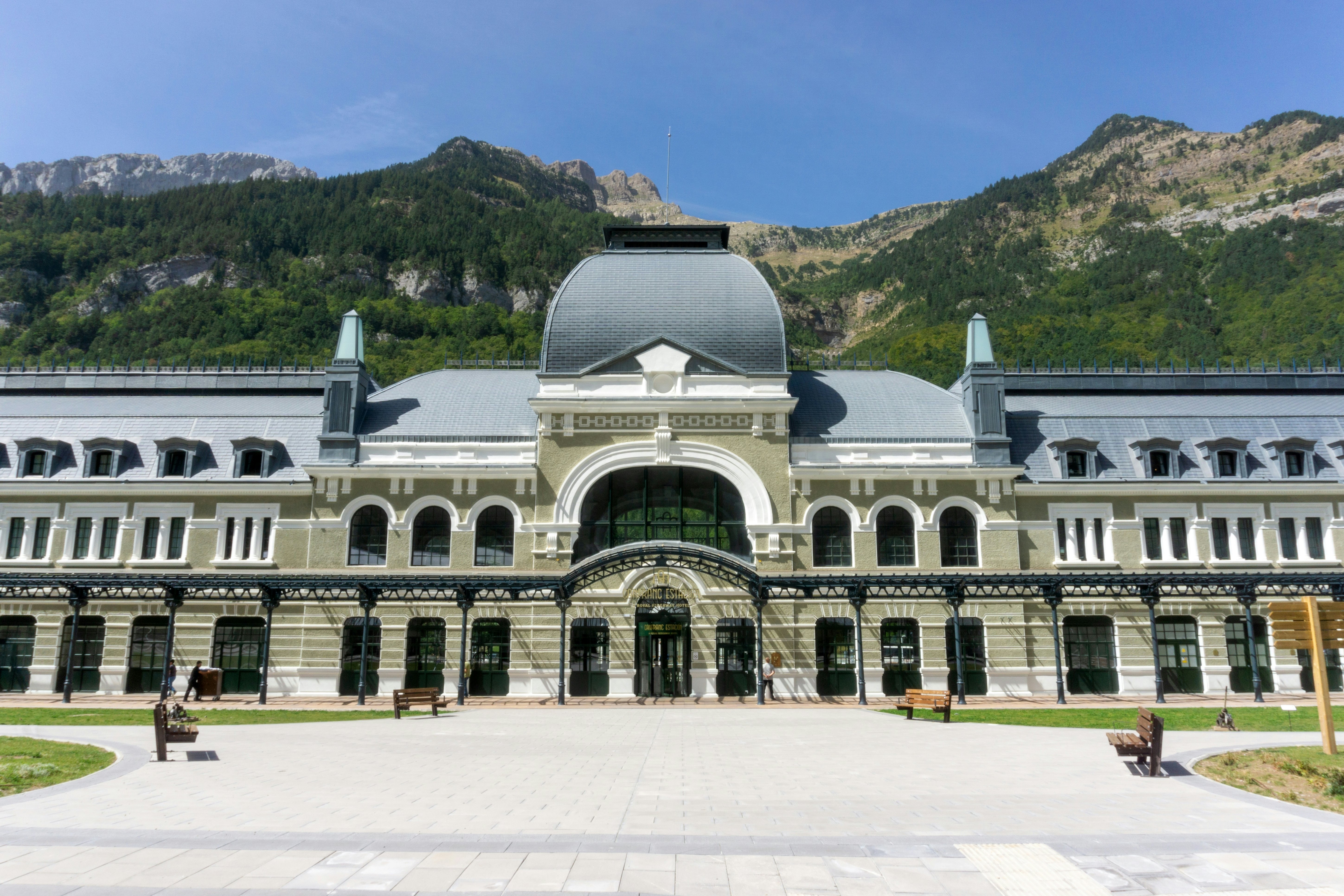 A vast train station building backed by mountains.