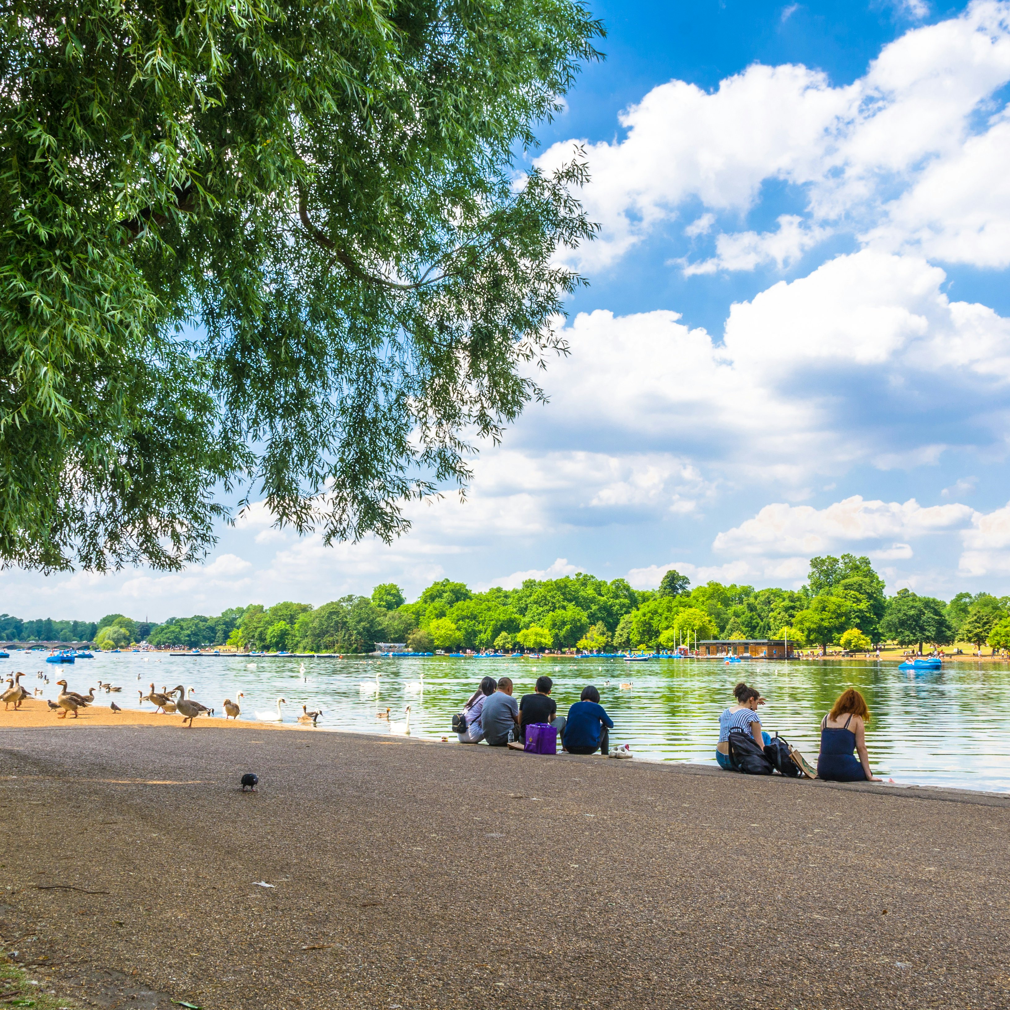 JUNE 18, 2017: Visitors seated on the shore of Serpentine Lake in Hyde Park.